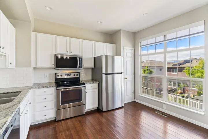 Kitchen with stainless steel appliances, light stone countertops, and white cabinetry