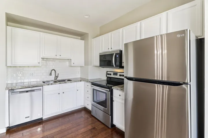Kitchen with stainless steel appliances, white cabinets, backsplash, and dark wood-type flooring