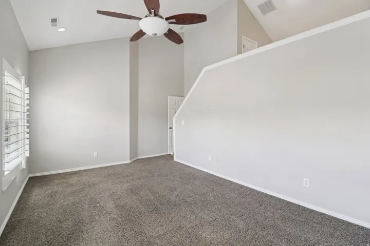 Empty room featuring vaulted ceiling, a ceiling fan, and dark colored carpet
