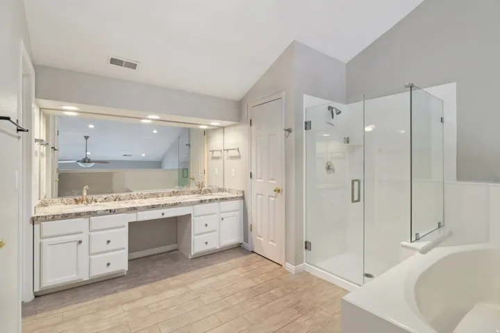 Bathroom featuring double vanity, a bath, light wood-style flooring, a stall shower, and vaulted ceiling