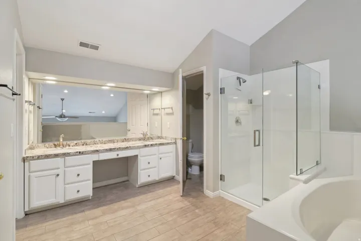 Full bath featuring double vanity, a garden tub, light wood finished floors, a stall shower, and vaulted ceiling