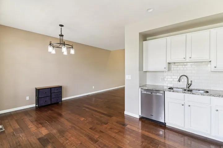 Kitchen featuring dishwasher, white cabinets, dark wood-type flooring, and light stone countertops