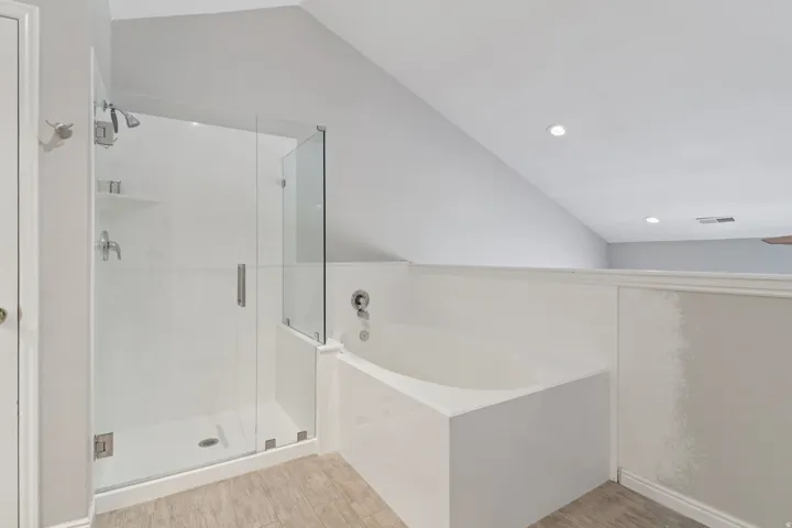 Full bath with vaulted ceiling, a garden tub, a stall shower, and light wood-type flooring