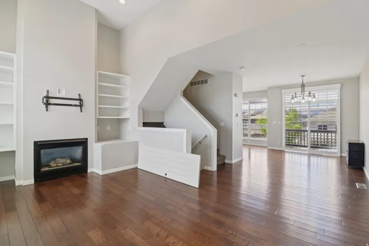 Unfurnished living room with dark wood-type flooring, suspended lighting, a glass covered fireplace, and built in features