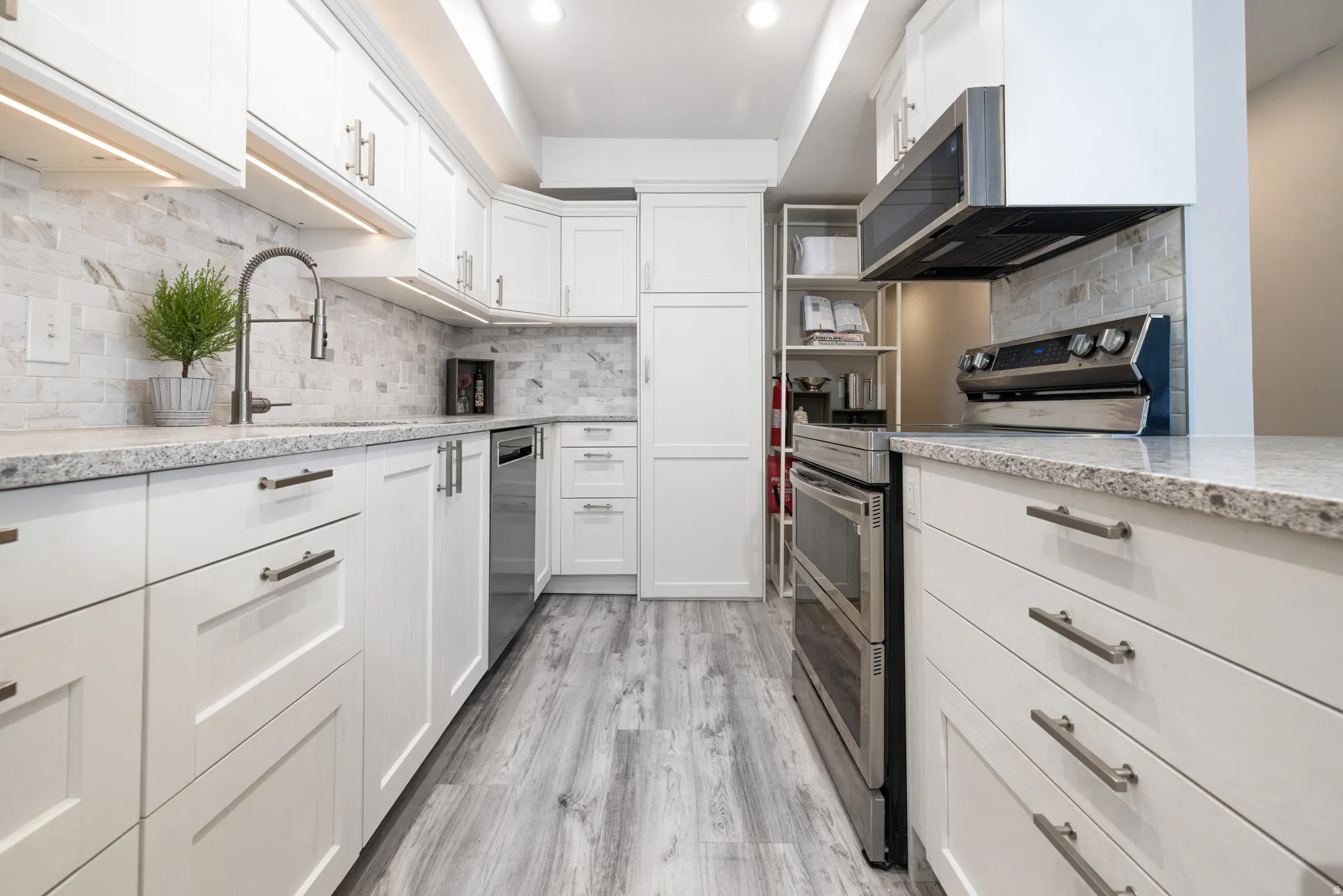 Kitchen featuring stainless steel appliances, white cabinetry, light stone countertops, tasteful backsplash, and open shelves