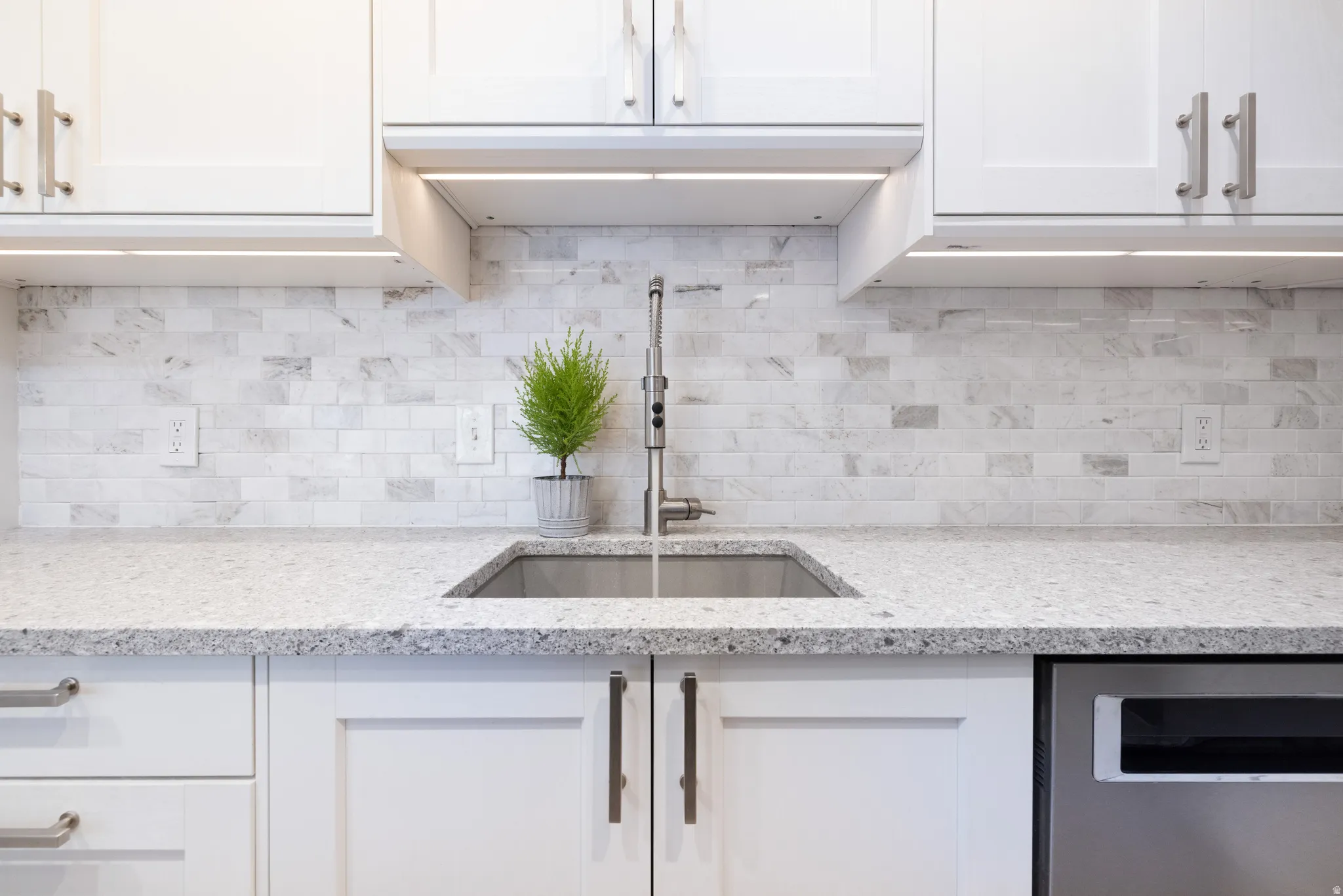 Kitchen with white cabinets, light stone counters, and dishwasher