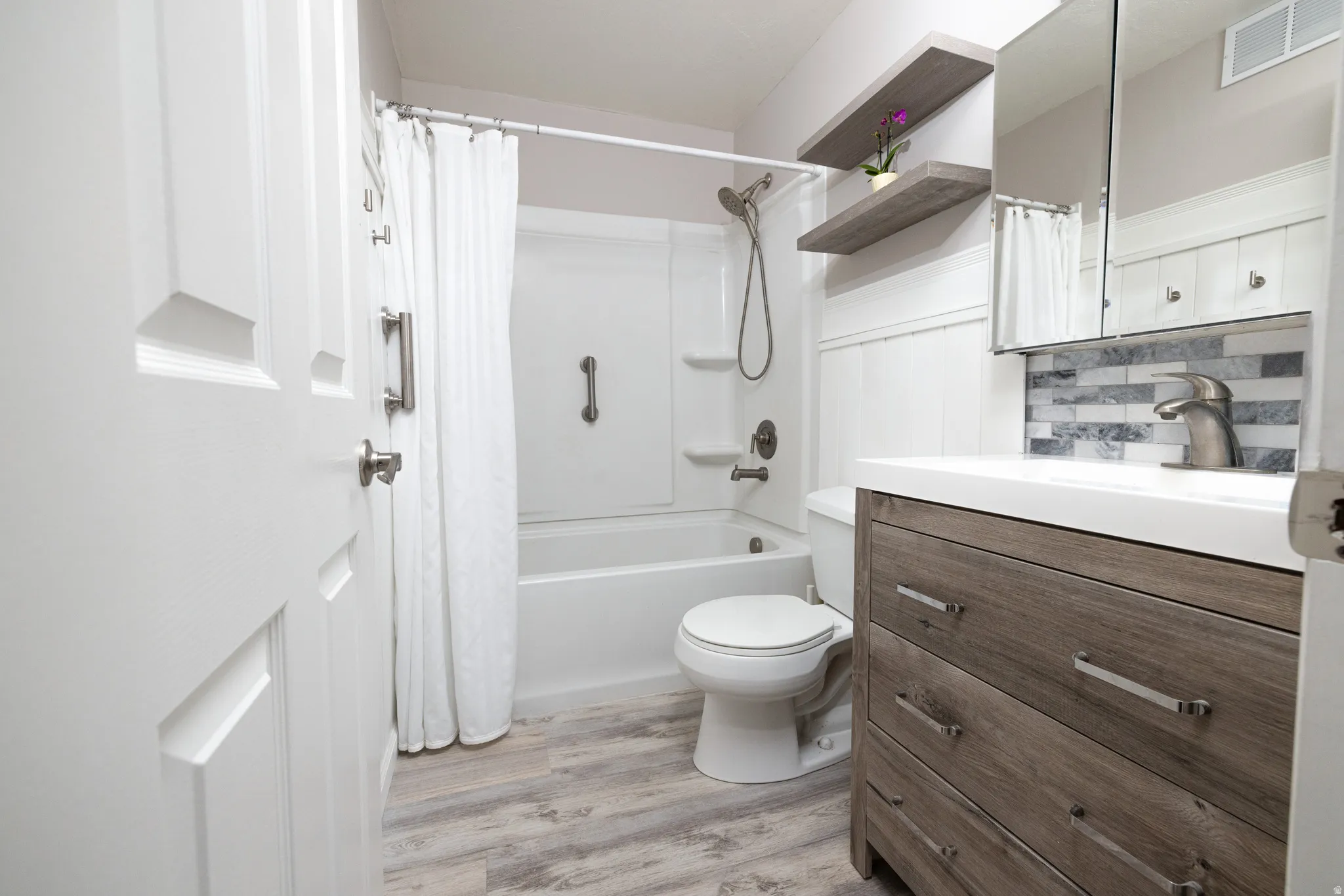 Bathroom featuring vanity, light wood-type flooring, shower / bathtub combination with curtain, and decorative backsplash