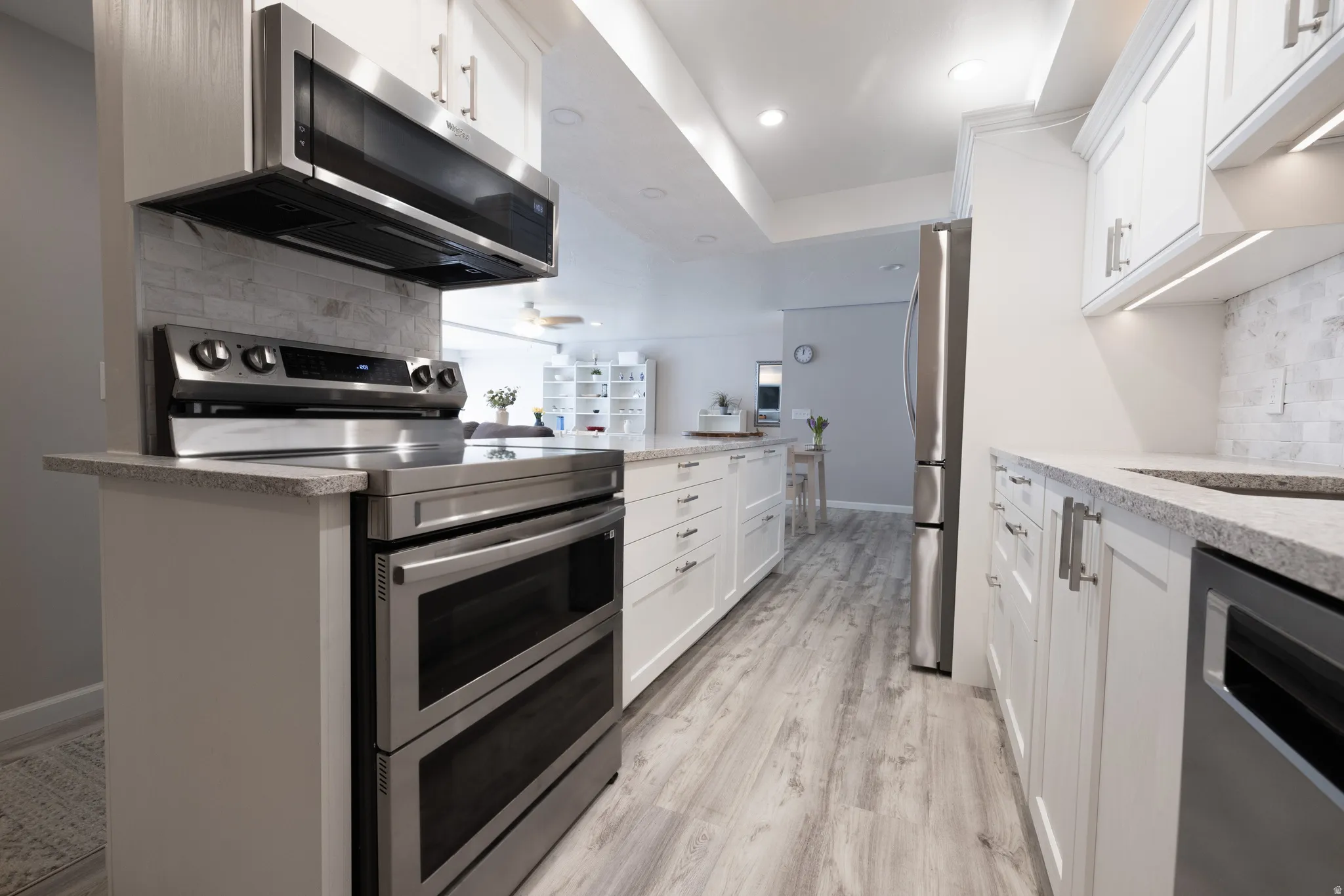 Kitchen featuring stainless steel appliances, decorative backsplash, white cabinets, and light stone countertops