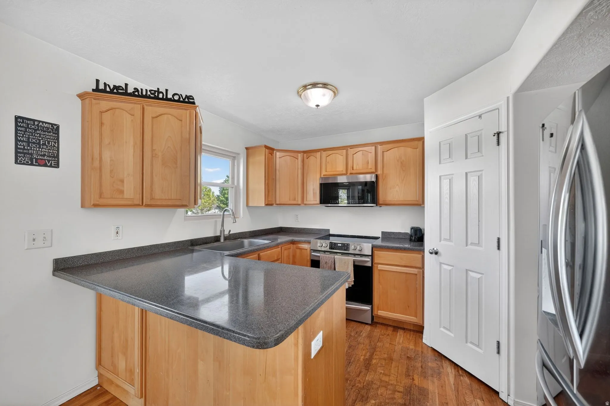 Kitchen with a peninsula, stainless steel appliances, dark wood-style floors, and light wood finish cabinets
