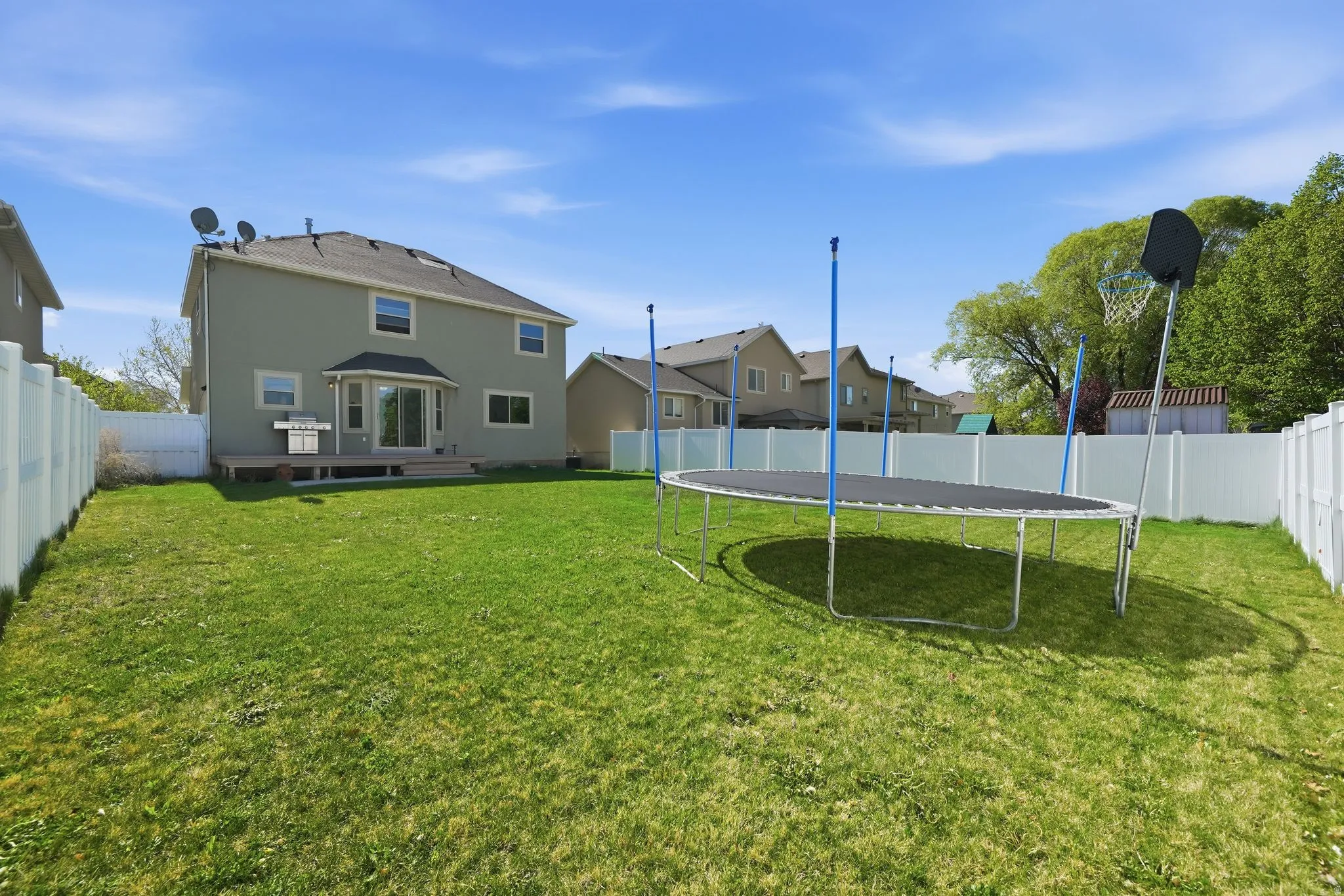 Rear view of property with a deck, a fenced backyard, a trampoline, and a residential view