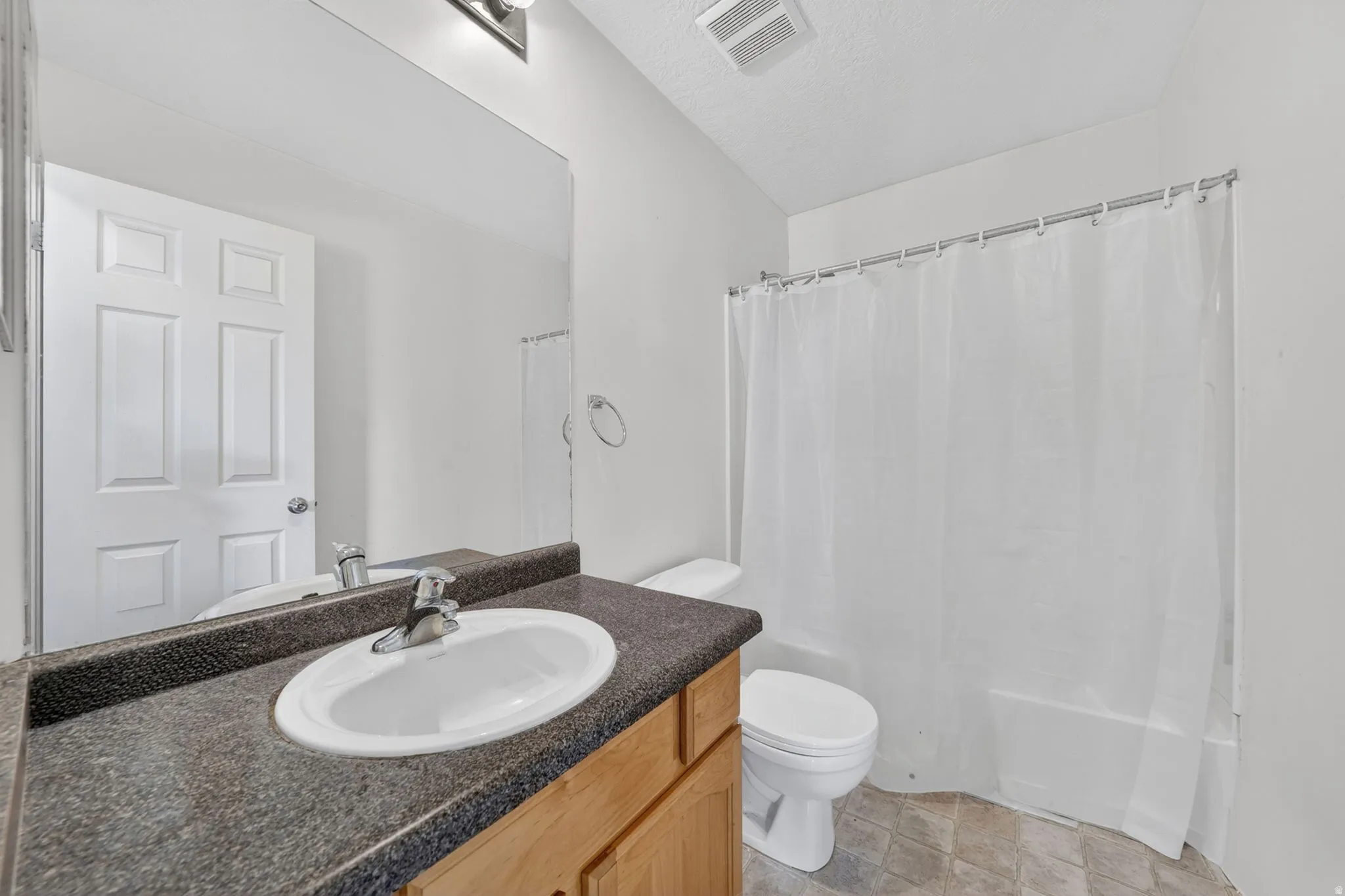 Full bathroom featuring vanity, shower / tub combo with curtain, and a textured ceiling