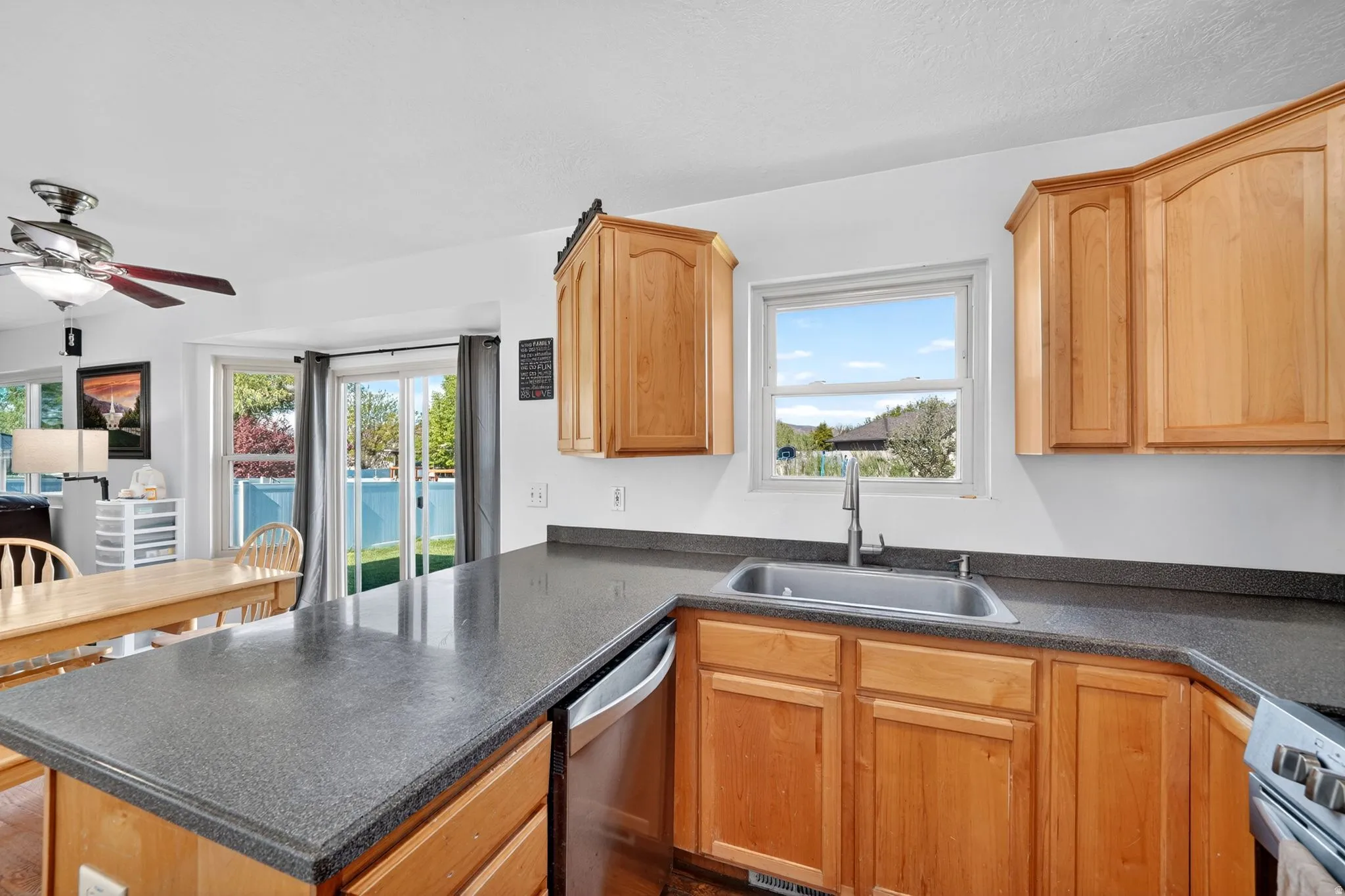 Kitchen featuring stainless steel appliances, a peninsula, dark countertops, a ceiling fan, and light wood finish cabinets