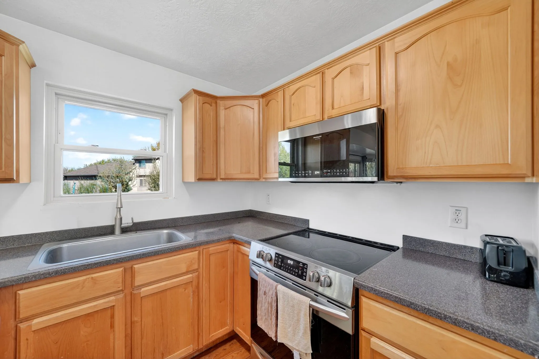 Kitchen with stainless steel appliances, light wood finish cabinets, and a textured ceiling