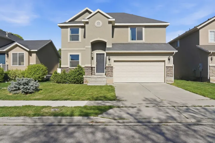 View of front of house featuring stone siding, a front yard, a garage, concrete driveway, and stucco siding