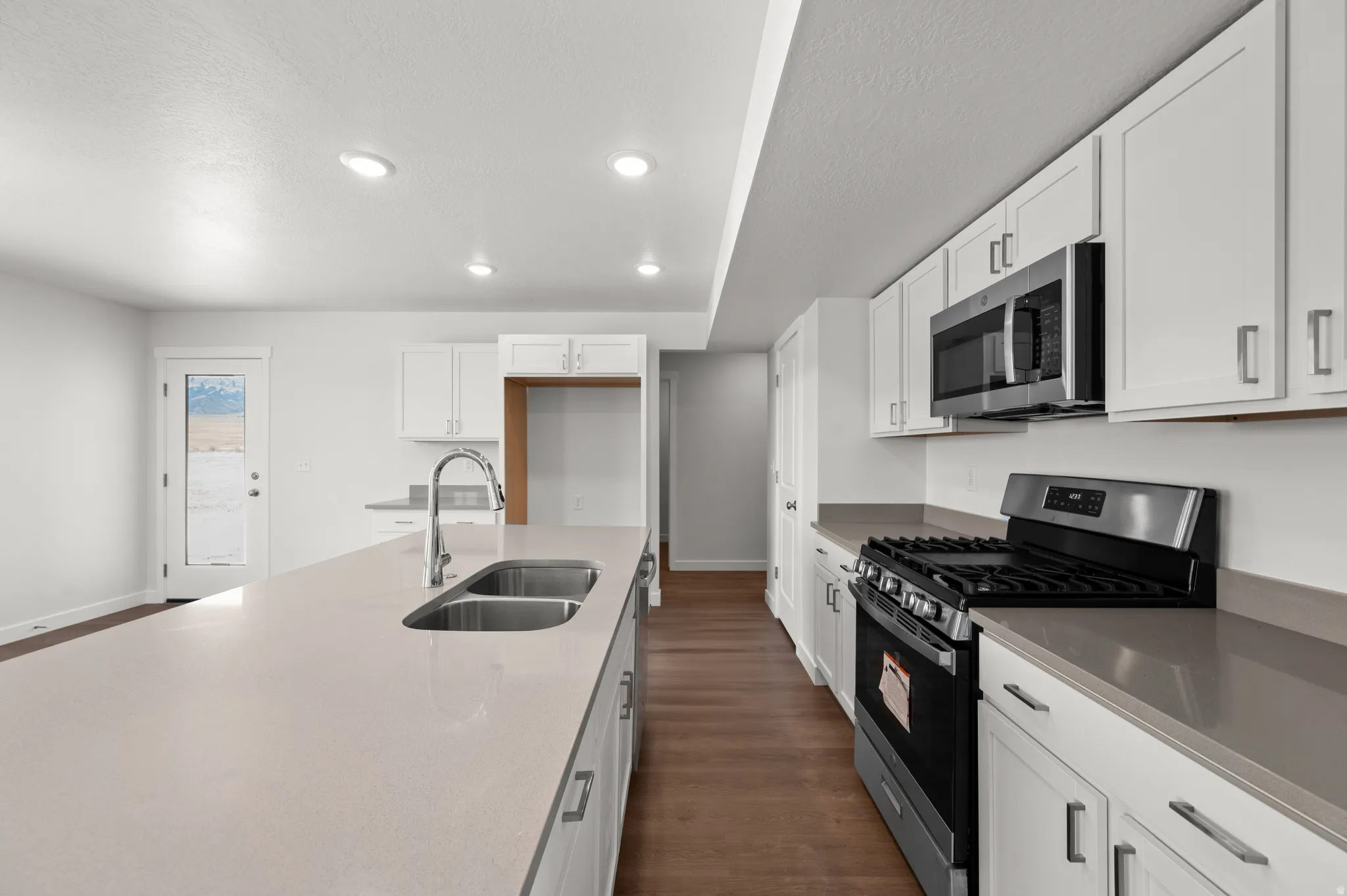 Kitchen featuring stainless steel appliances, white cabinetry, dark wood-style flooring, light stone countertops, and recessed lighting