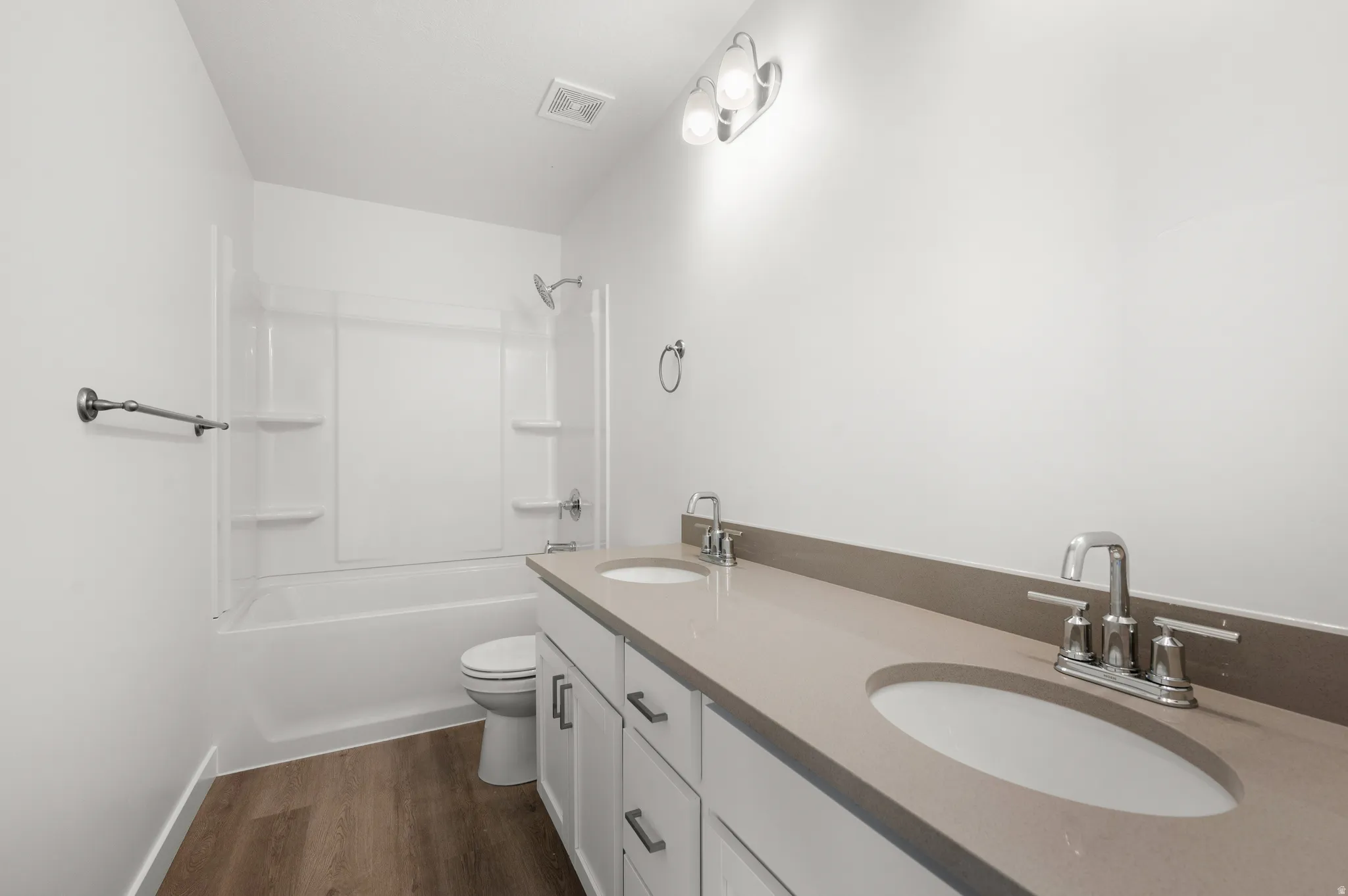 Full bathroom featuring double vanity, dark wood-style flooring, and bathing tub / shower combination