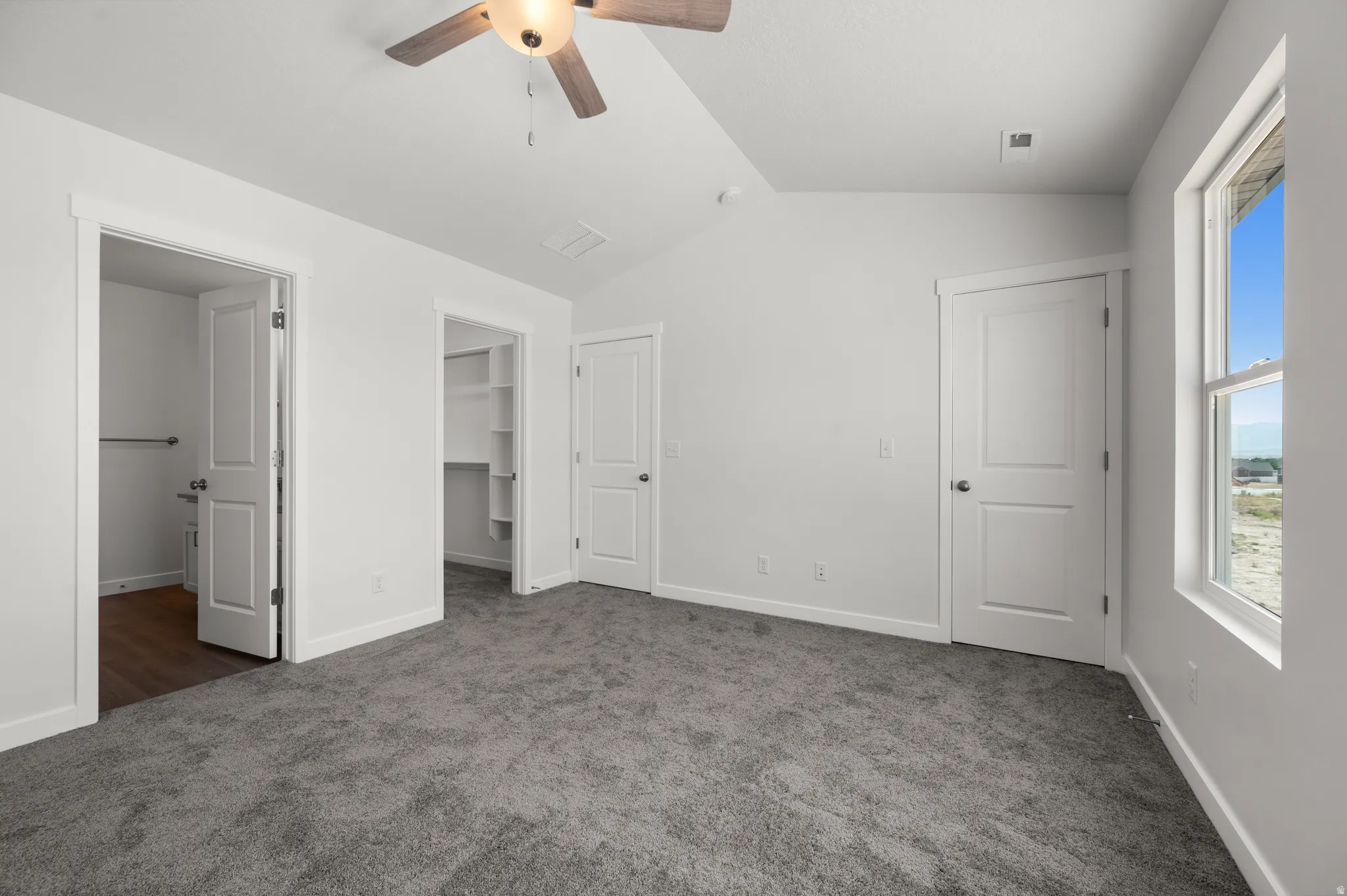 Unfurnished bedroom featuring a walk in closet, dark carpet, and ceiling fan