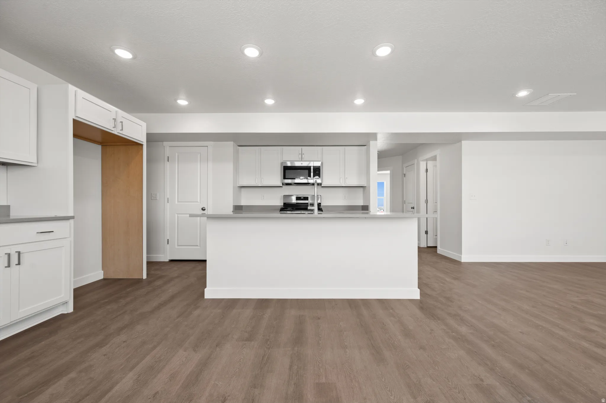 Kitchen with white cabinetry, stainless steel appliances, a center island with sink, light countertops, and dark wood-style flooring