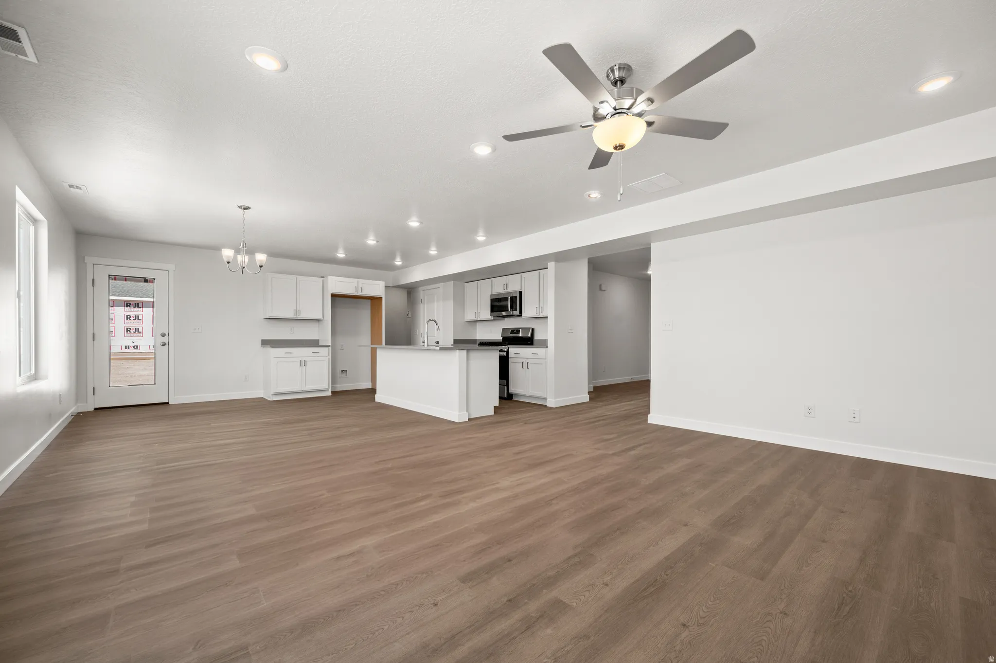 Unfurnished living room with suspended lighting, ceiling fan, and dark wood-style floors