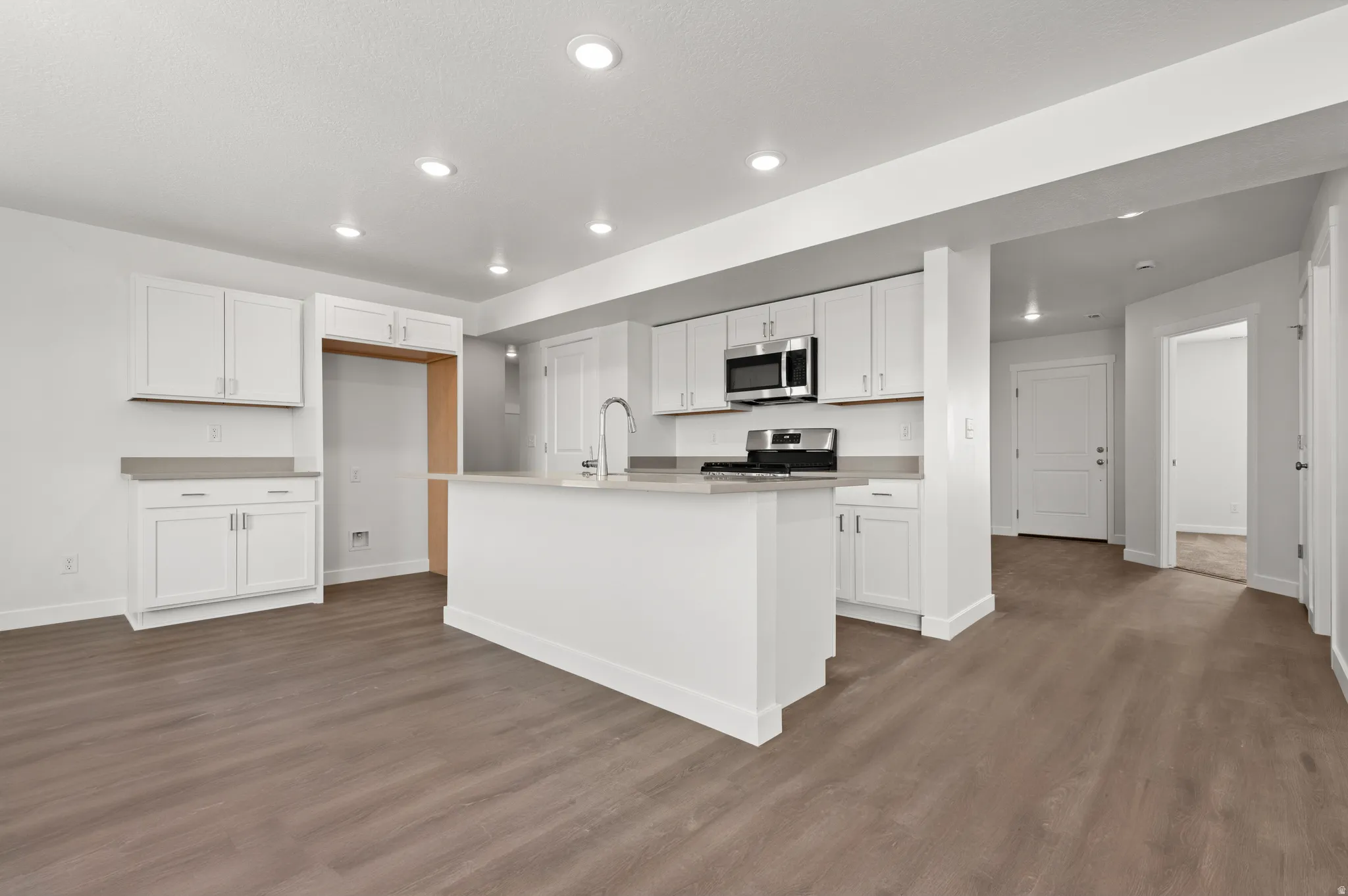 Kitchen featuring white cabinets, a center island with sink, dark wood finished floors, stainless steel appliances, and recessed lighting