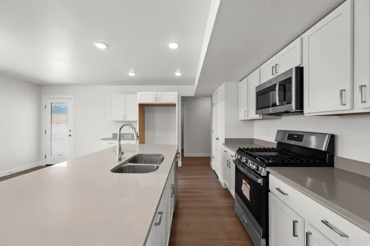 Kitchen featuring stainless steel appliances, white cabinetry, dark wood-style flooring, light stone countertops, and recessed lighting