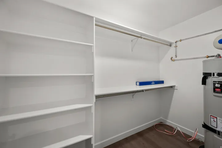 Walk in closet with dark wood-style flooring and water heater
