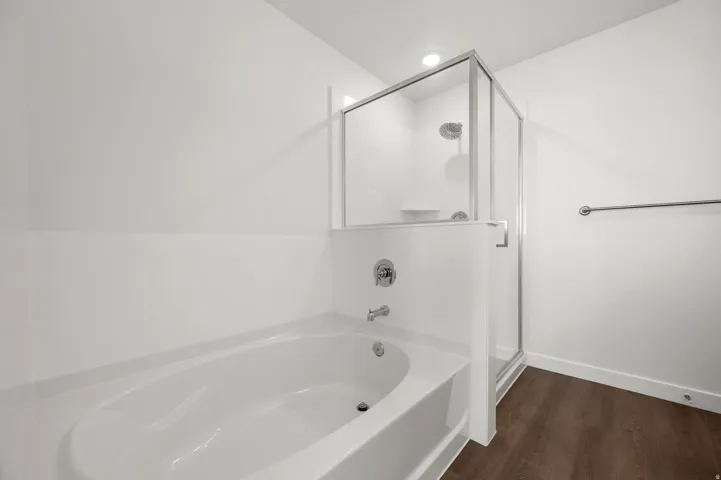 Full bathroom featuring a bath, a shower stall, and dark wood-type flooring
