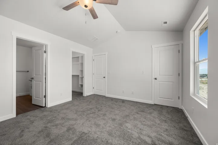 Unfurnished bedroom featuring a walk in closet, dark carpet, and ceiling fan