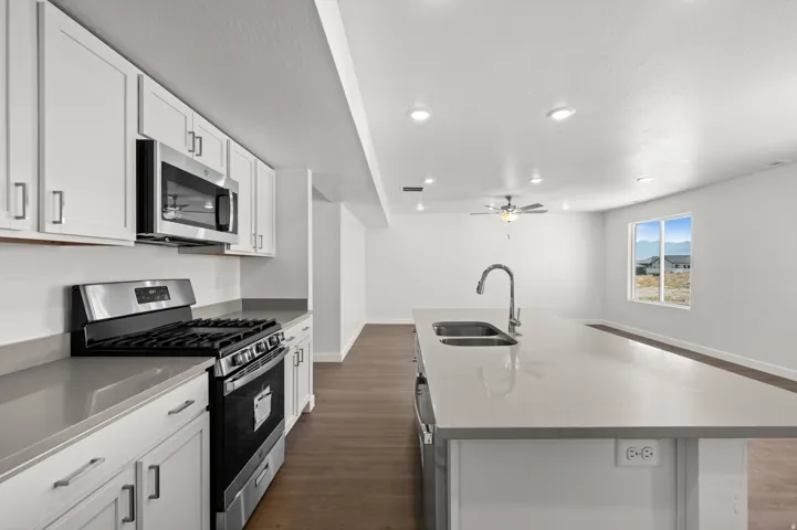 Kitchen with stainless steel appliances, dark wood-style flooring, white cabinetry, a center island with sink, and a ceiling fan