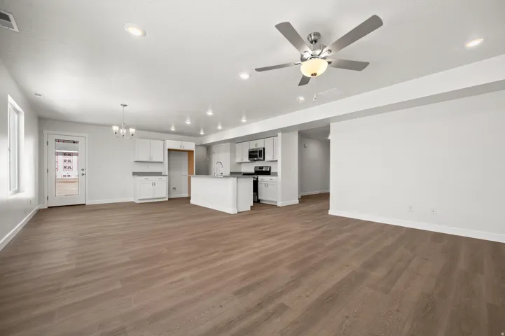 Unfurnished living room with suspended lighting, ceiling fan, and dark wood-style floors