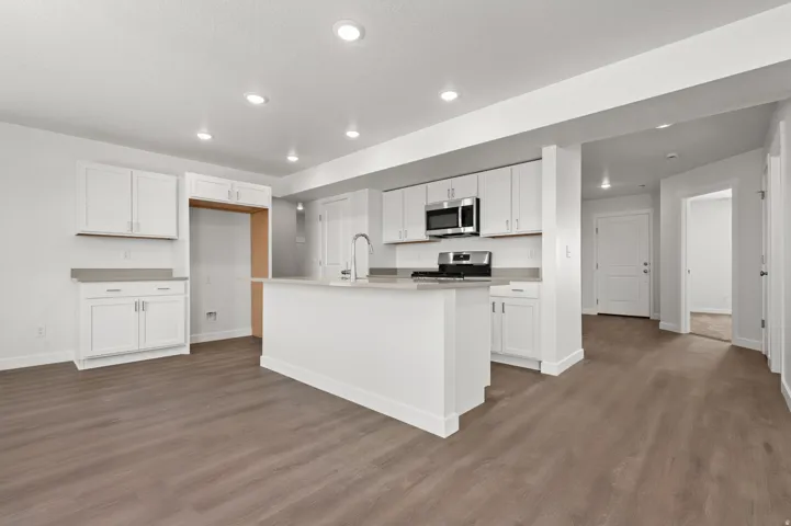 Kitchen featuring white cabinets, a center island with sink, dark wood finished floors, stainless steel appliances, and recessed lighting