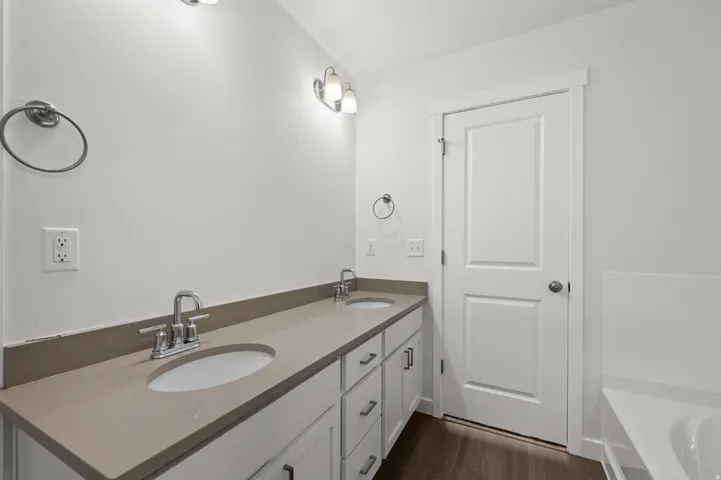 Bathroom featuring double vanity, a bath, and dark wood finished floors