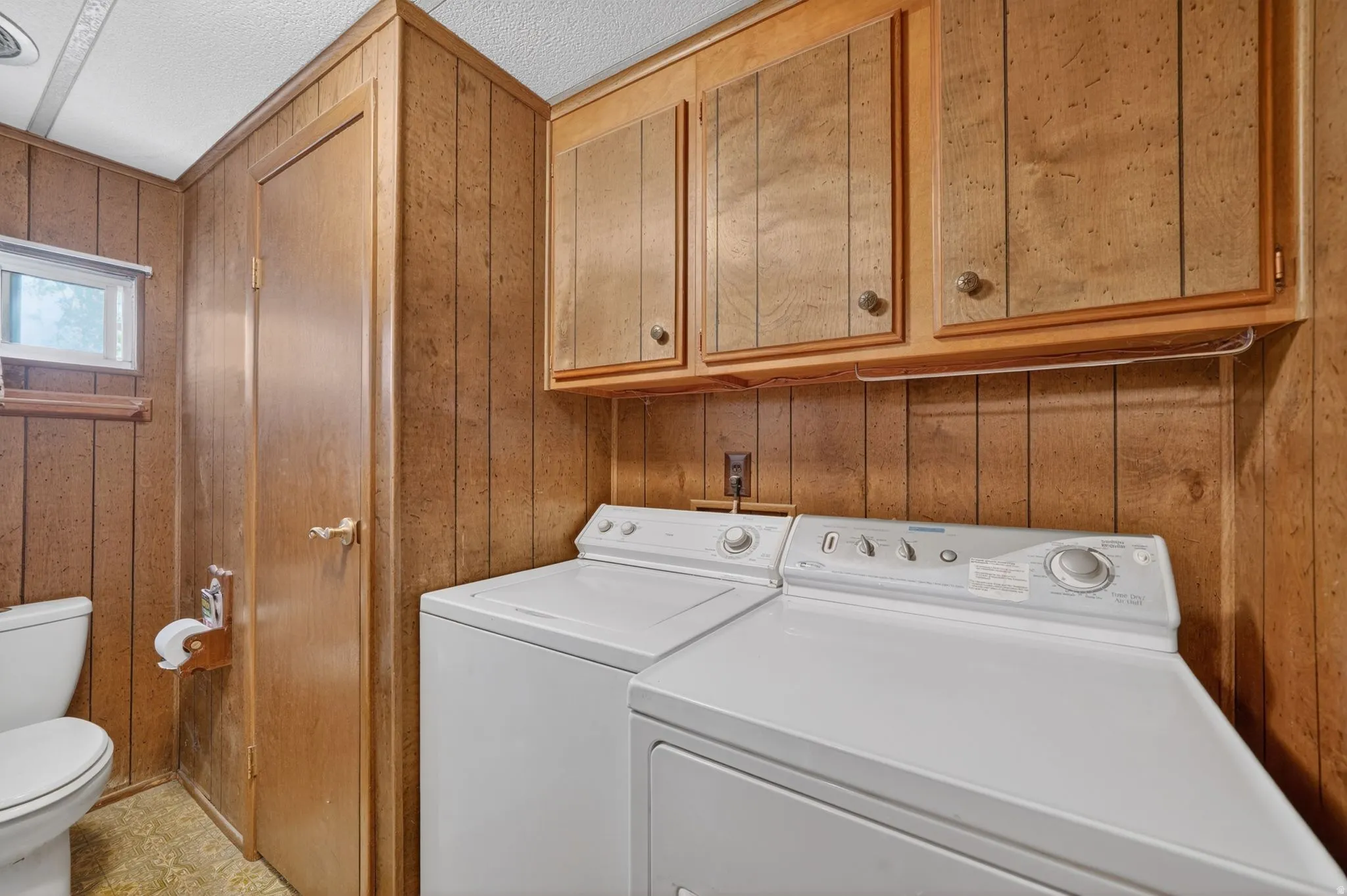 Laundry room featuring wooden walls, a textured ceiling, and washer and clothes dryer