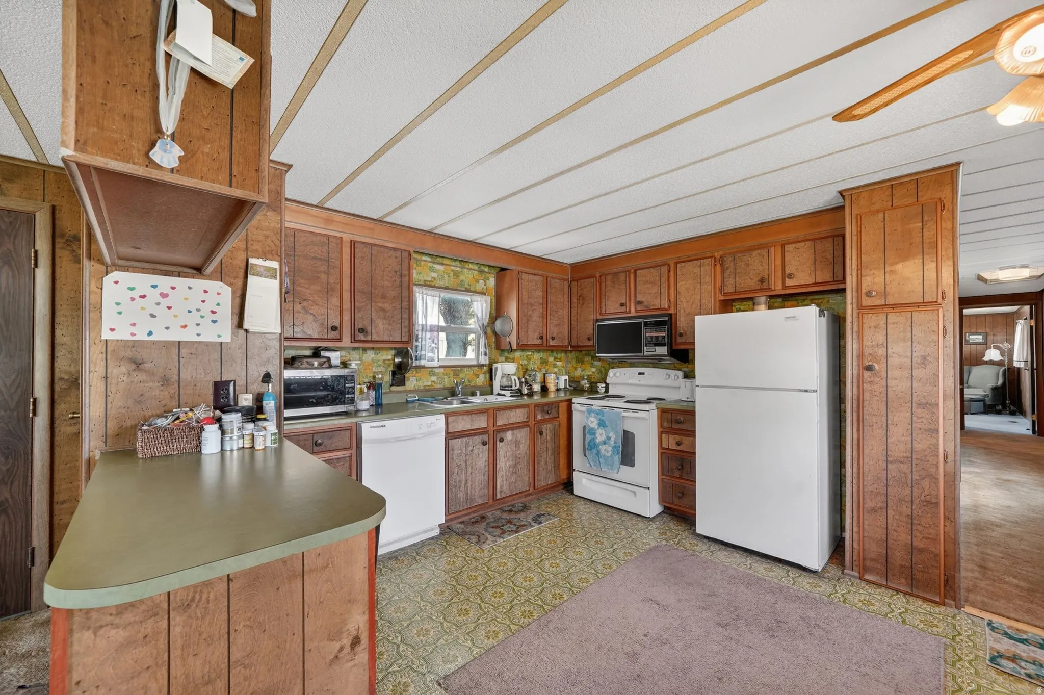 Kitchen featuring light flooring, white appliances, wood finish cabinetry, wooden walls, and ceiling fan