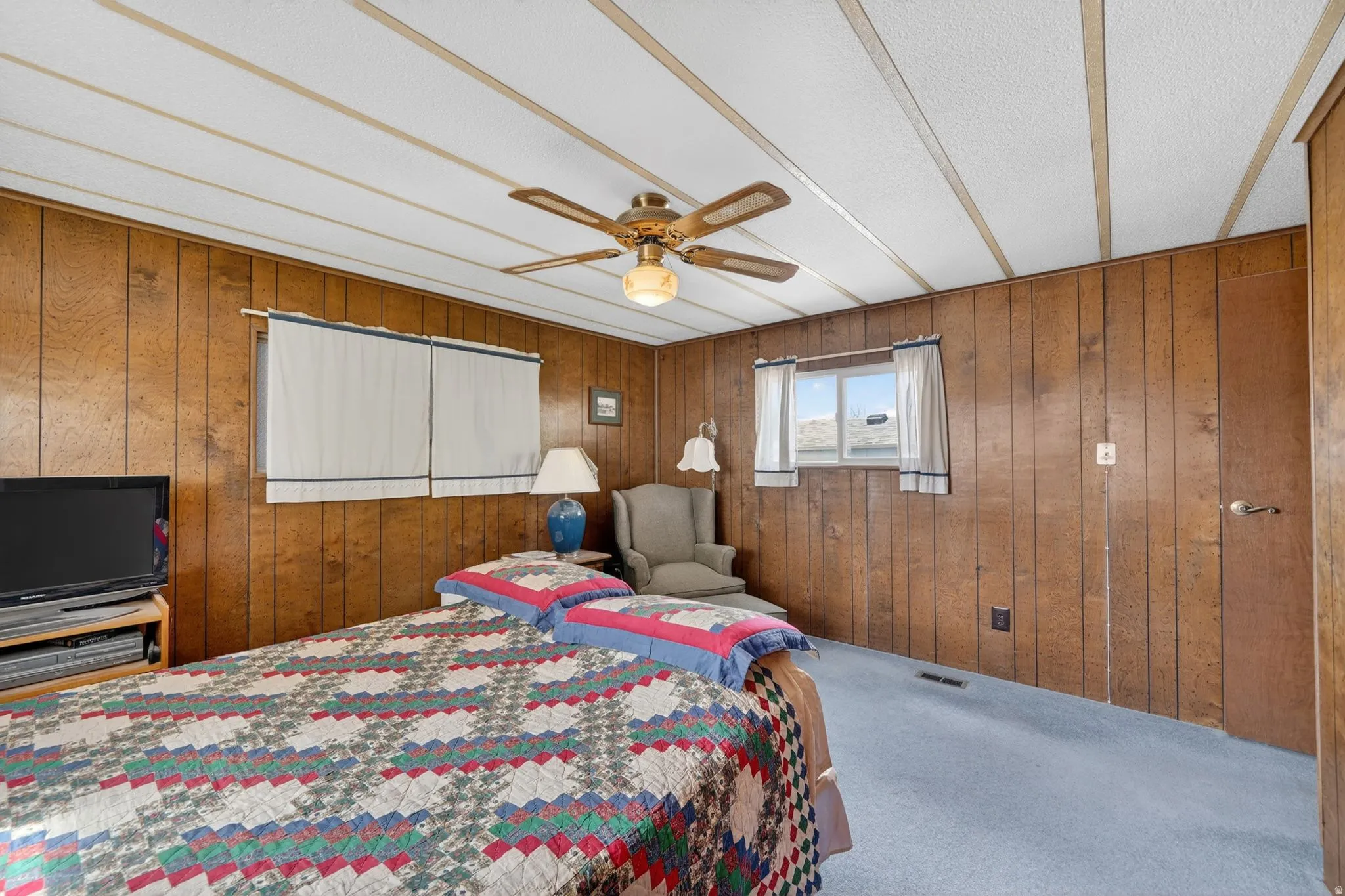 Bedroom featuring wooden walls, carpet, a ceiling fan, and a textured ceiling