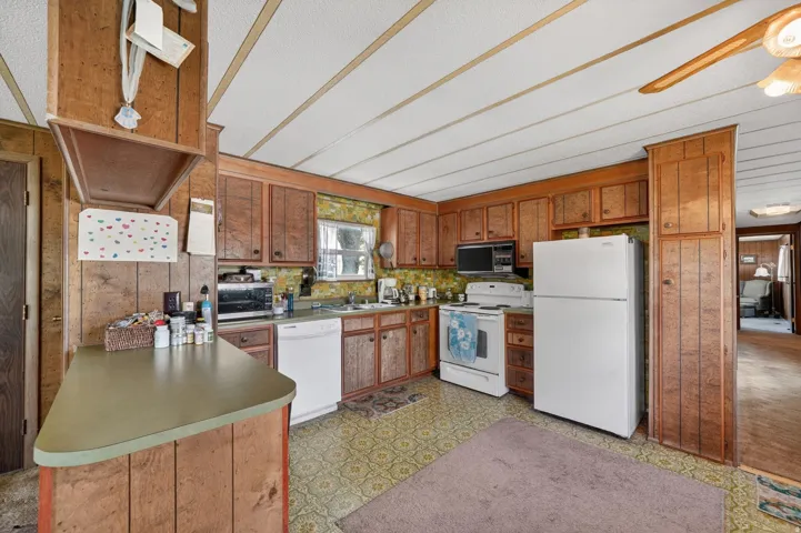 Kitchen featuring light flooring, white appliances, wood finish cabinetry, wooden walls, and ceiling fan