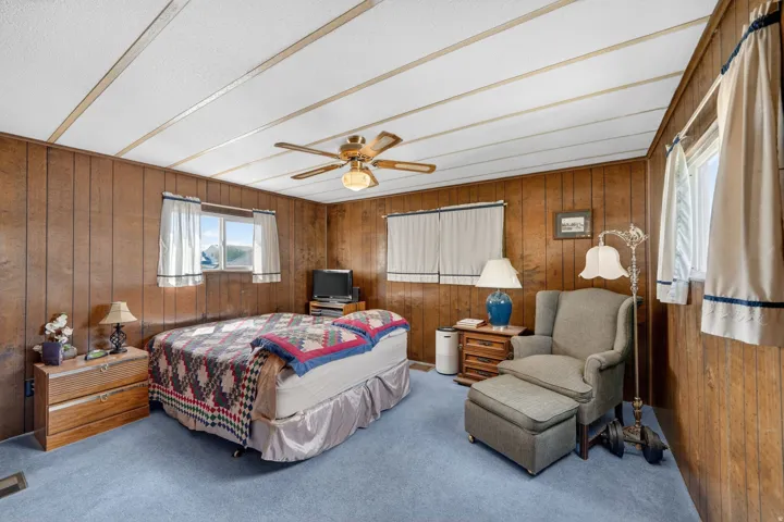 Bedroom with wooden walls, light carpet, and a ceiling fan