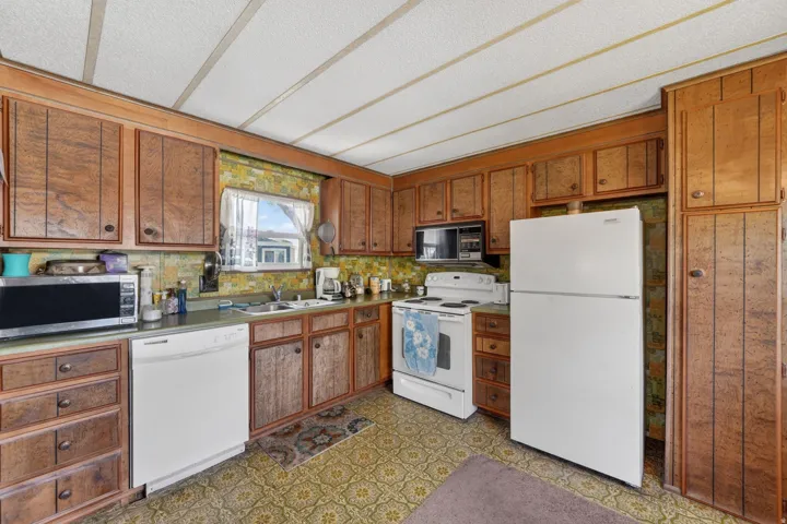 Kitchen with white appliances, wood finish cabinetry, dark floors, and light countertops