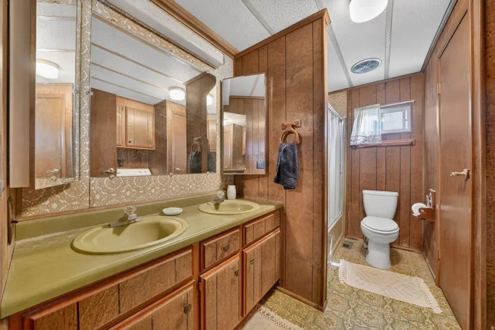 Full bath with shower / bath combo with shower curtain, double vanity, a textured ceiling, and wooden walls