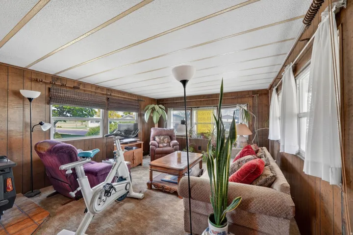 Sunroom with wooden walls, a textured ceiling, carpet floors, and a wood stove