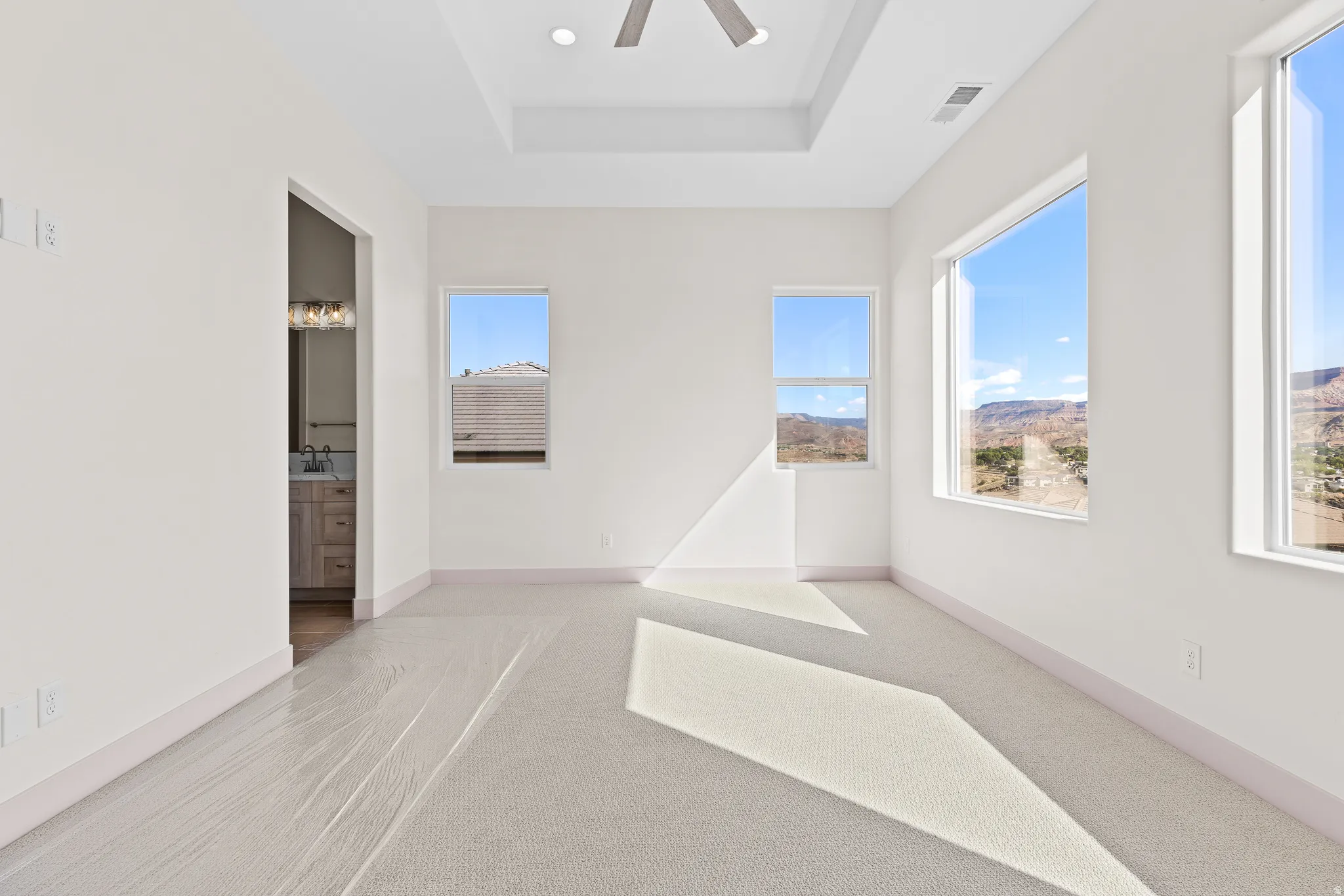 Unfurnished bedroom featuring light carpet, a tray ceiling, ceiling fan, ensuite bath, and recessed lighting