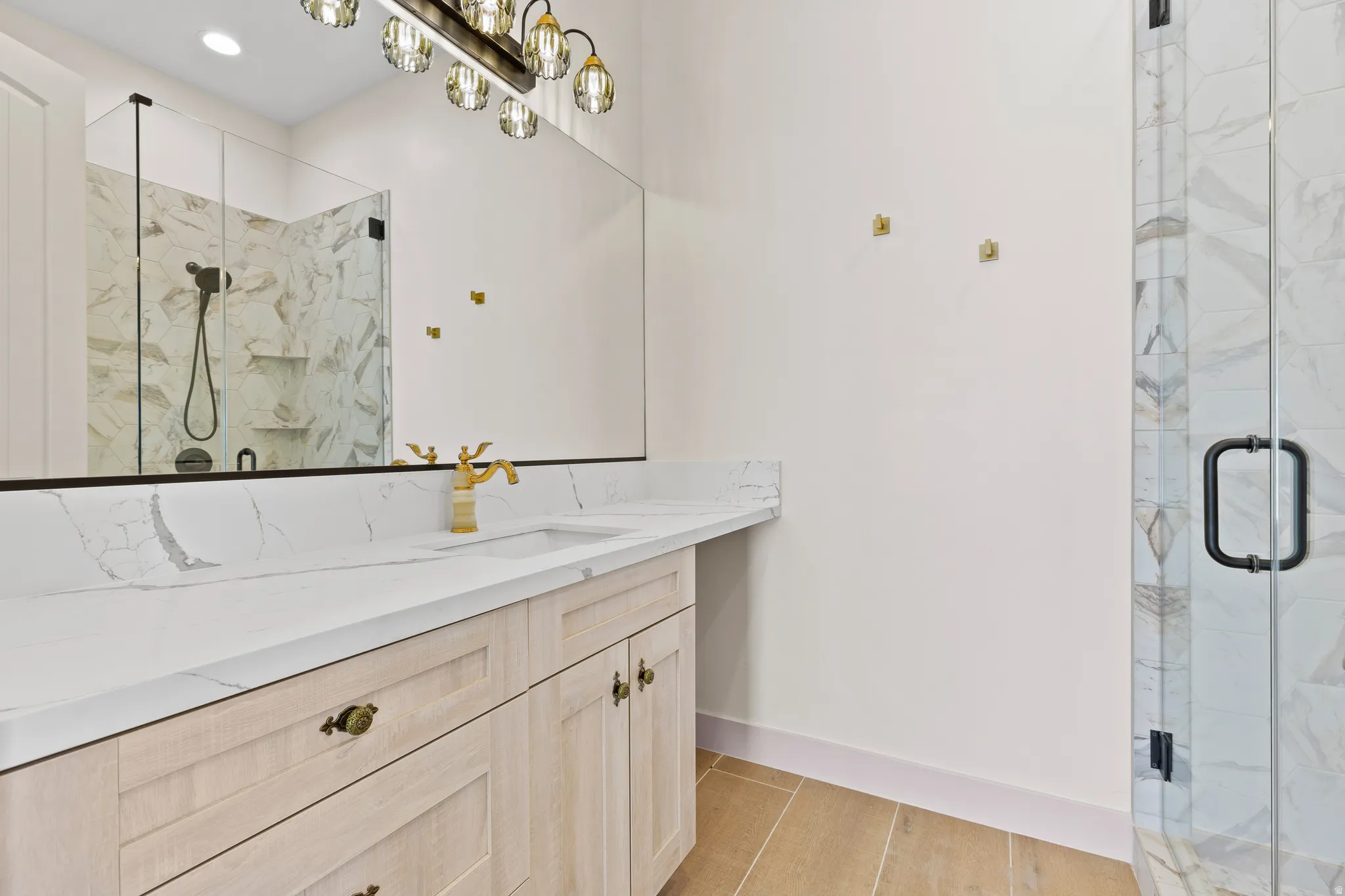 Full bath with vanity, a marble finish shower, light wood finished floors, and recessed lighting