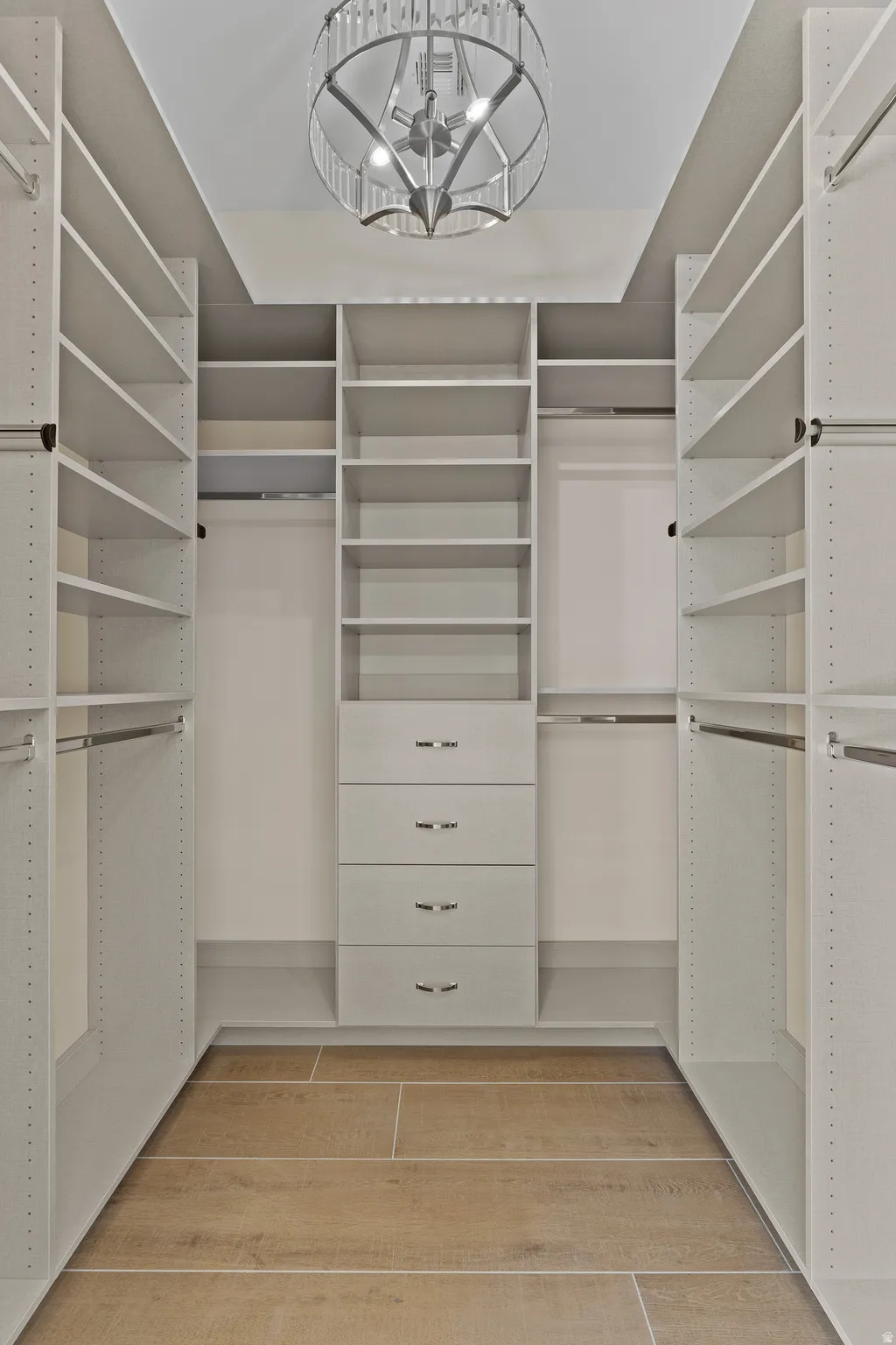 Walk in closet with light wood-style floors and hanging lights