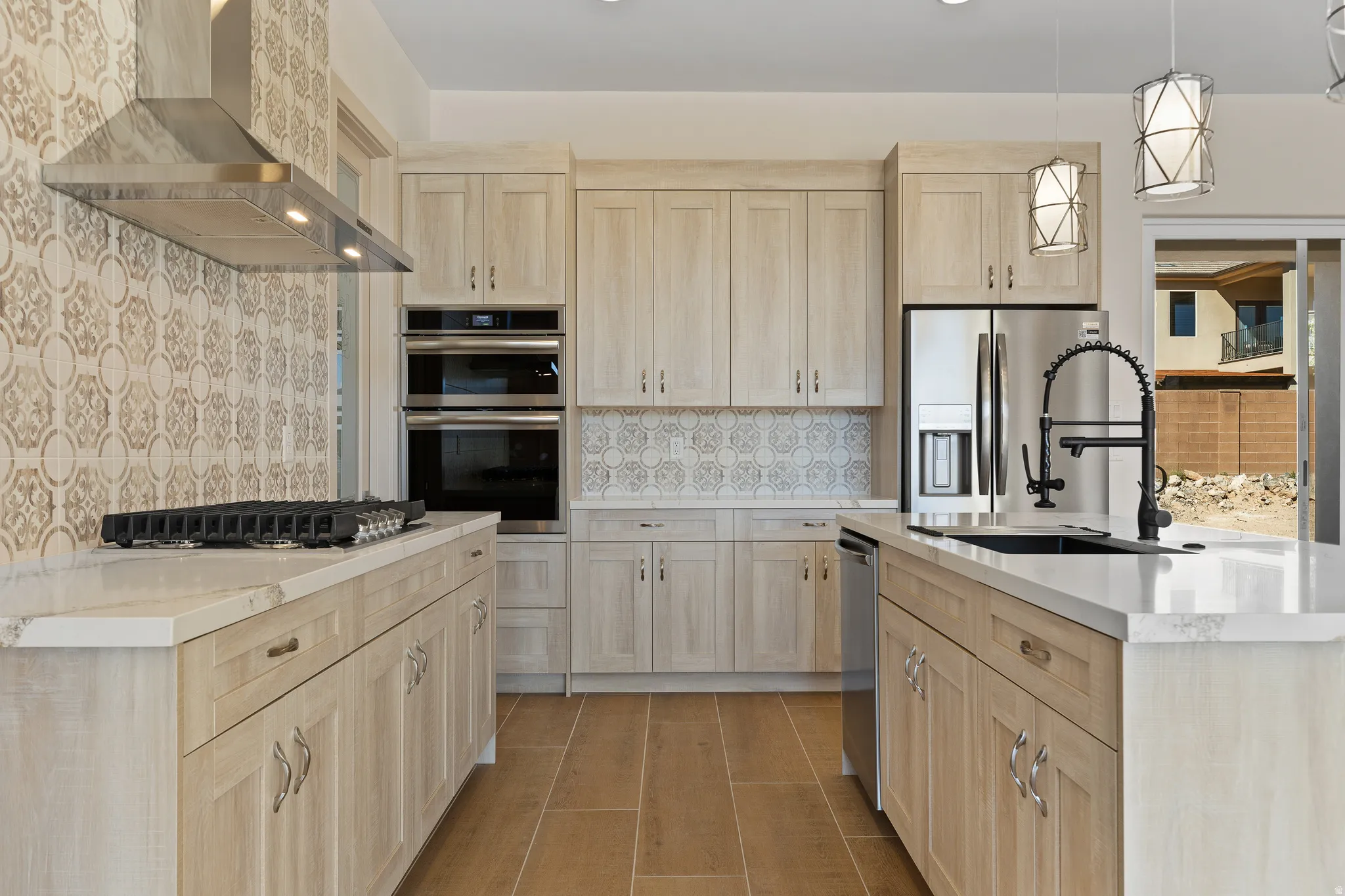 Kitchen featuring light wood finish cabinetry, stainless steel appliances, light stone counters, and backsplash