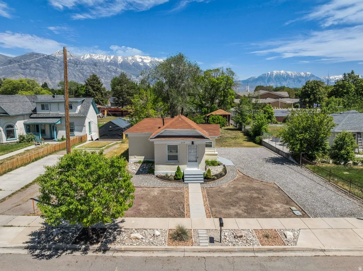 Single-story residence featuring a front walkway, established landscaping, a gravel driveway, and a mountain backdrop