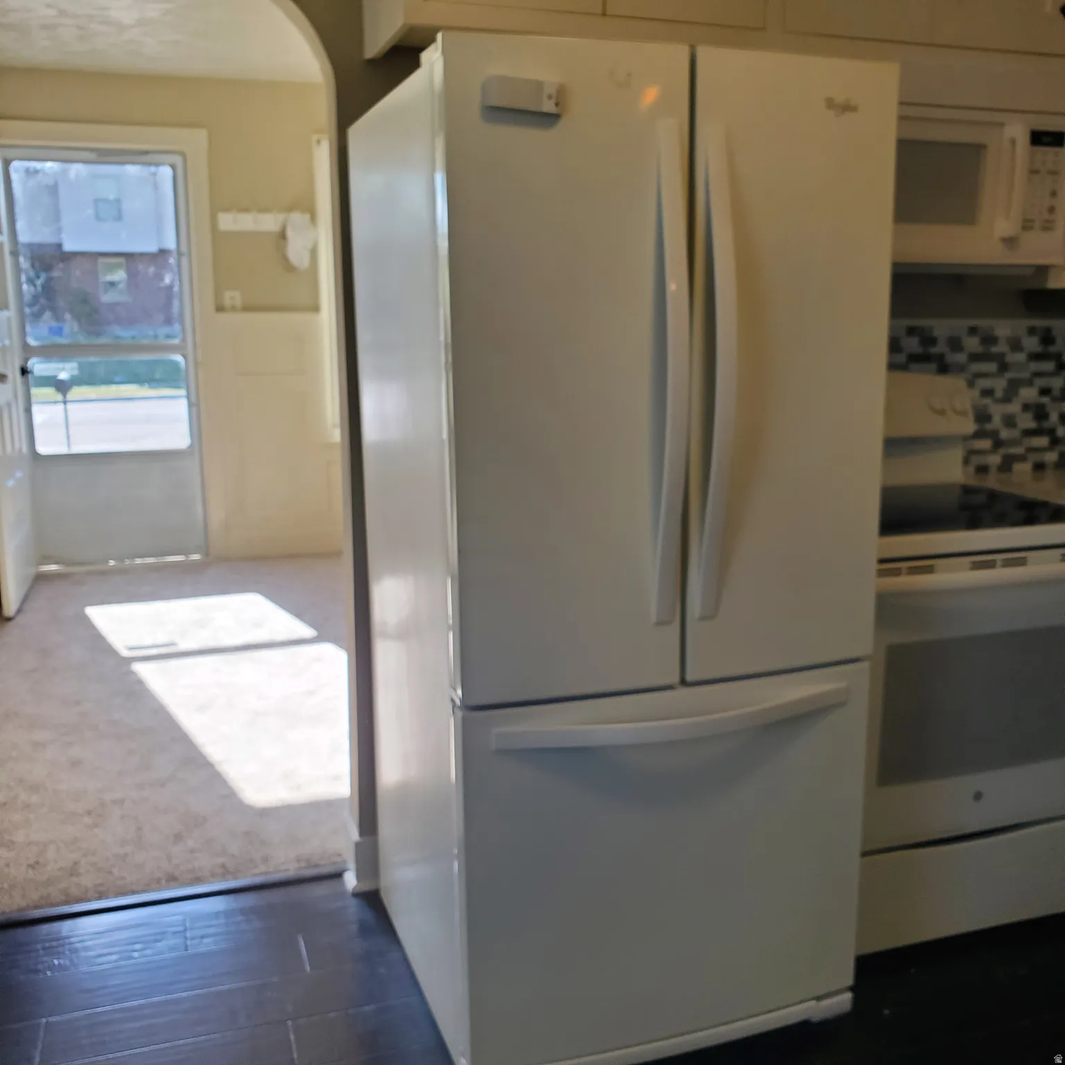 Kitchen with white appliances, arched walkways, dark wood-type flooring, white cabinetry