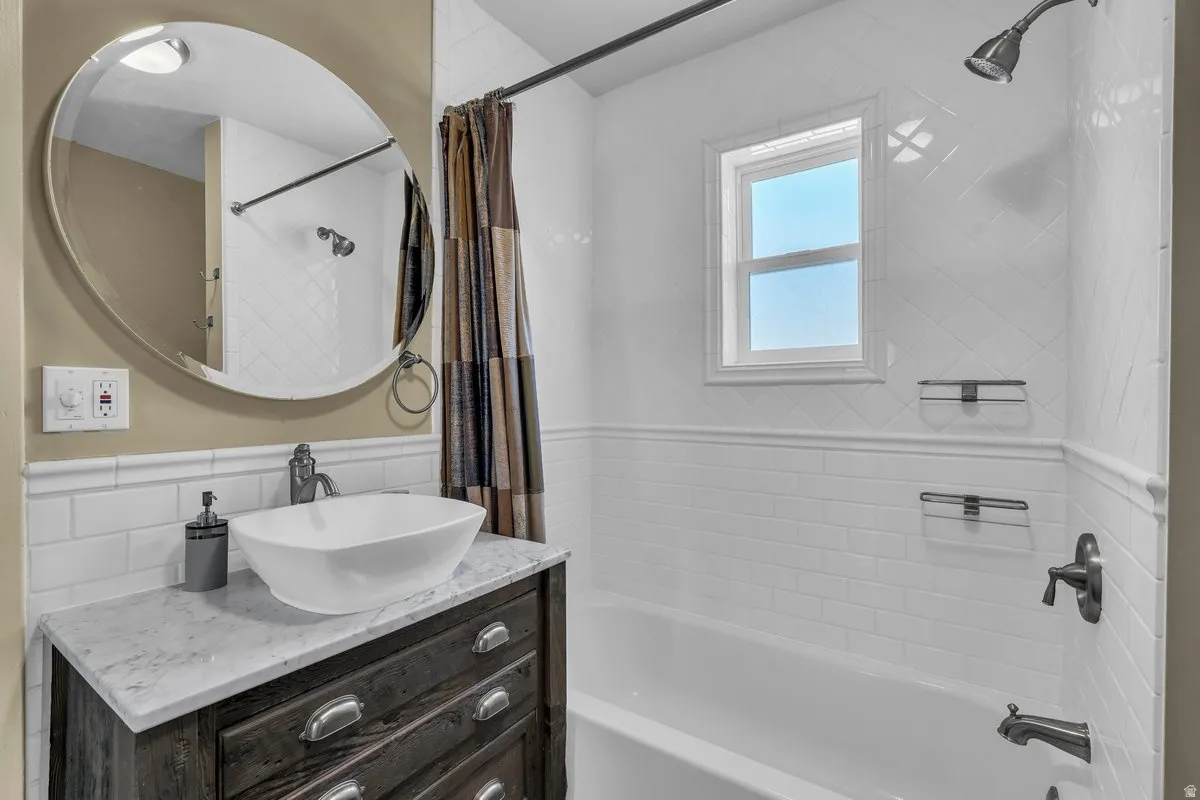 Bathroom featuring a freestanding vessel sink set on a wood-finish vanity with drawer pulls, a round mirror, and a white subway tile surround for the tub and shower