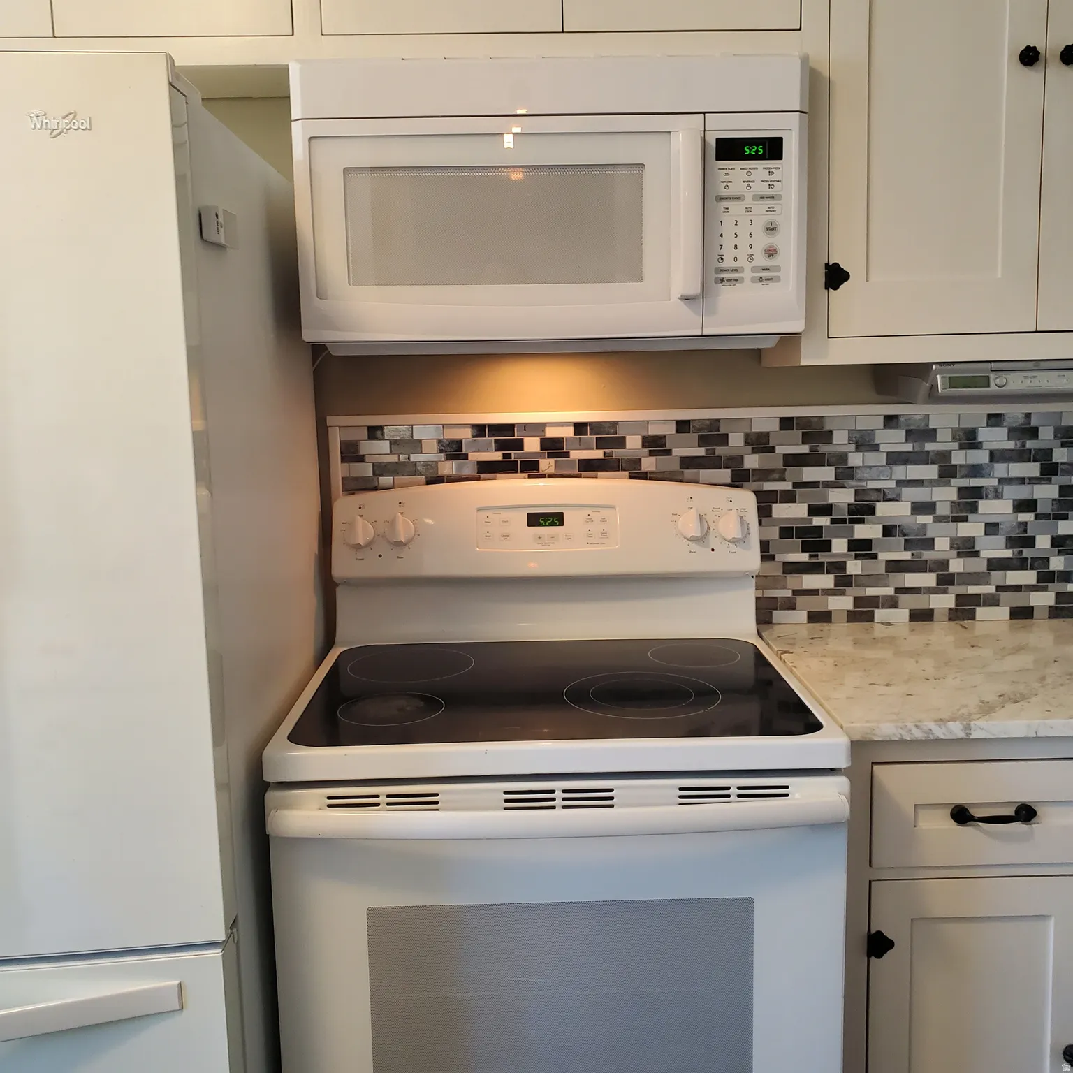 Kitchen with white appliances, decorative backsplash, white cabinets