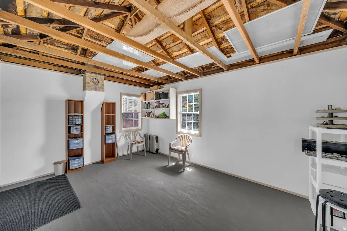 Open ceiling with exposed wood joists, white painted walls, and a gray floor finish