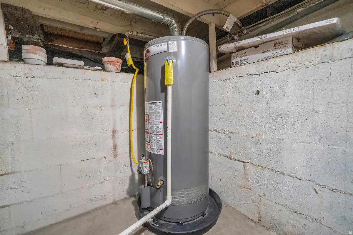 Utility area featuring a water heater with a drain pan, concrete block walls, and exposed ceiling joists